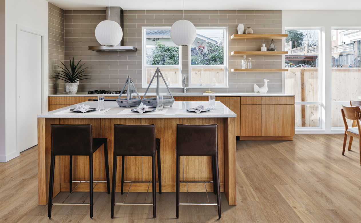 white stone countertops in kitchen with light waterproof hardwood floors and light wood modern cabinetry